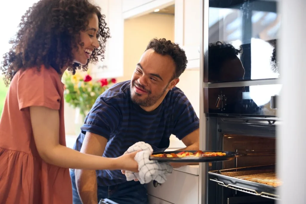 Disabled man with down syndrome and support worker baking pizza