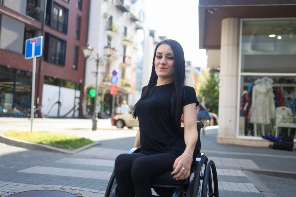 Smiling disabled woman in wheelchair crossing footpath